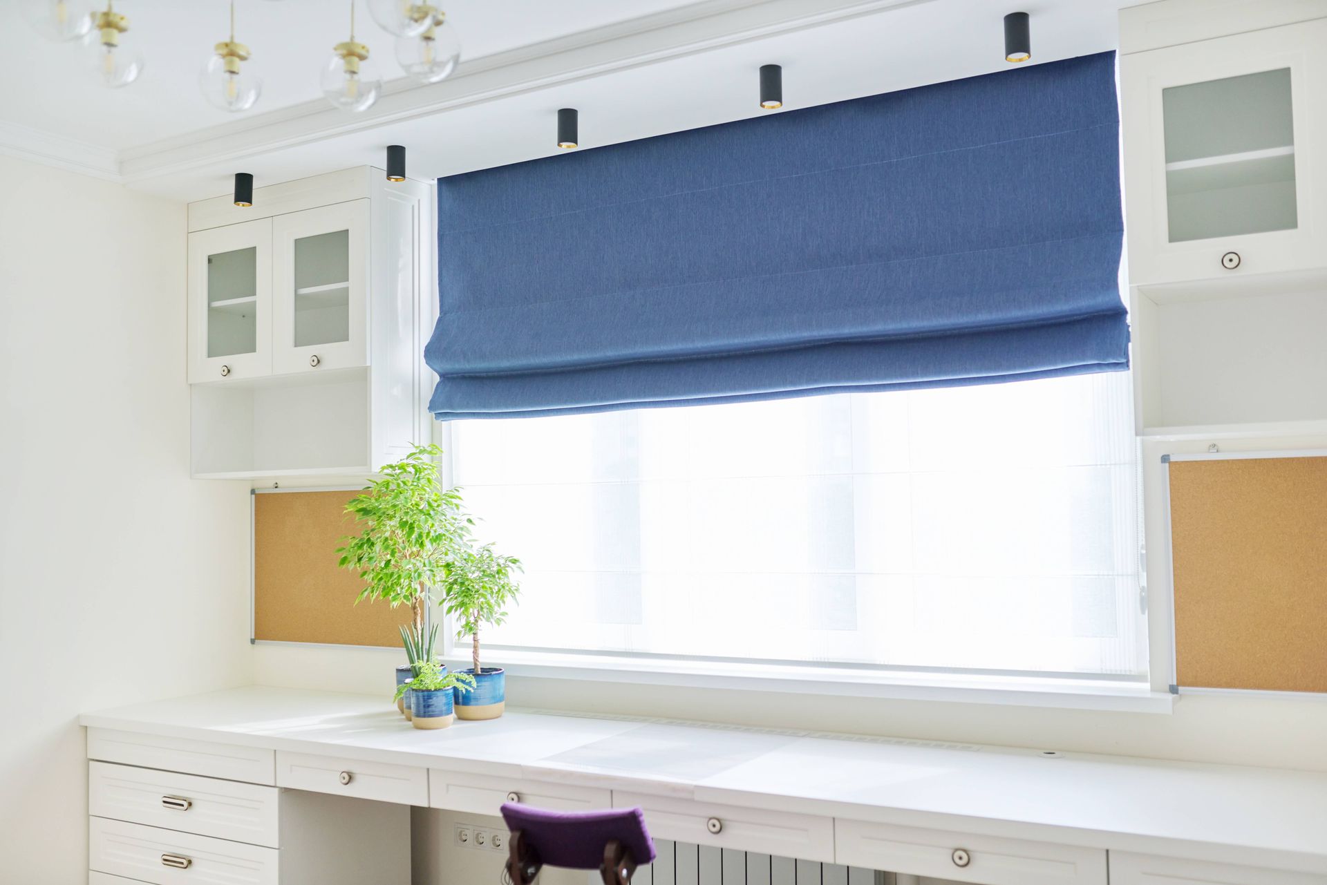 A blue Roman shade in a home office setup at Blinded by Delight Window Coverings & Design near Boern