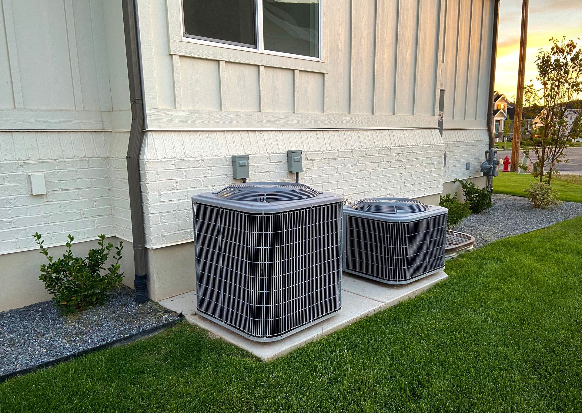 Two air conditioners are sitting on the side of a house.