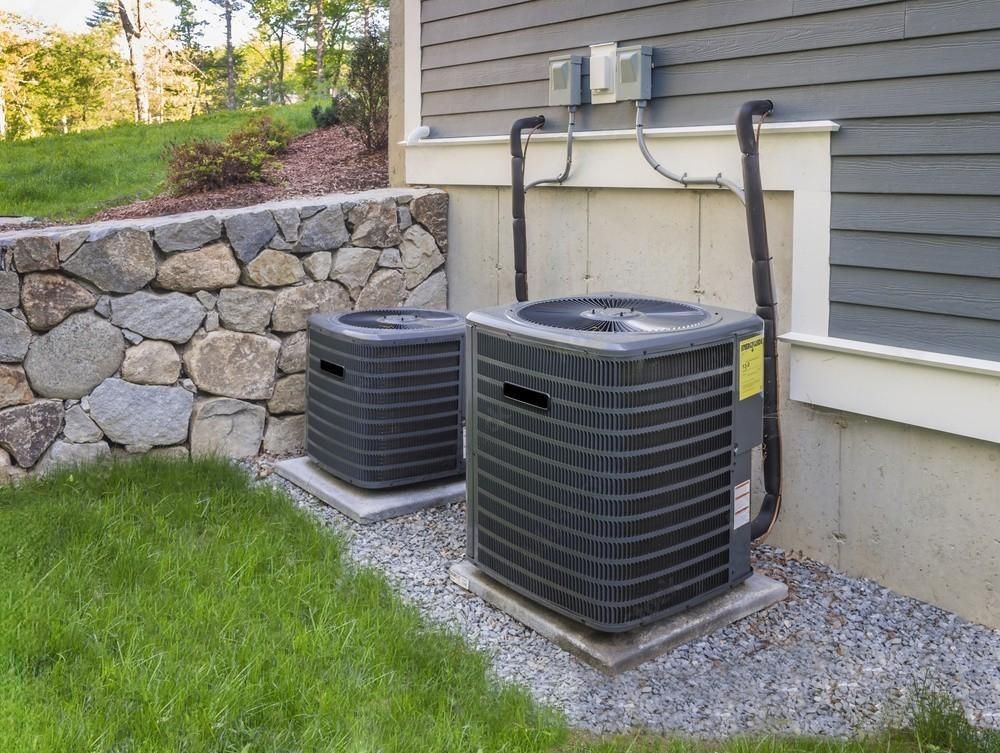 two air conditioners are sitting outside of a house next to a stone wall .
