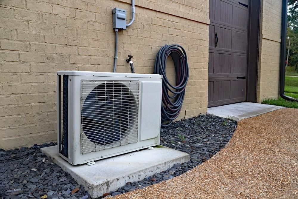 an air conditioner is sitting outside of a brick building next to a hose .