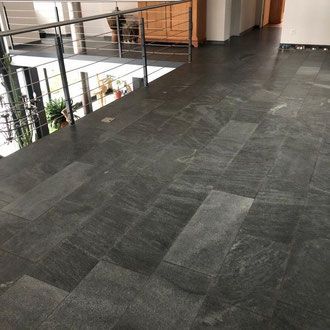 Dunkelgrauer Fliesenboden mit Metallgeländer, das auf eine tiefer gelegene Ebene blickt.