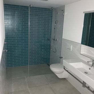 Modernes Badezimmer mit türkisfarbener Backstein-Duschwand, Glaskabine, schwebendem Waschbecken und Toilette.