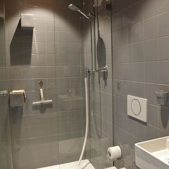 Grau geflieste Dusche mit Glastür und silberfarbenen Armaturen.