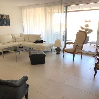 Helles Wohnzimmer mit weißen Möbeln, Zugang zur Terrasse und einem dekorativen Stuhl.