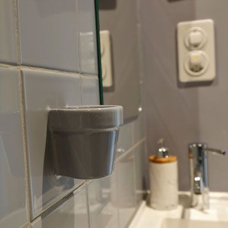 Grauer Keramik-Zahnbürstenhalter an der gefliesten Badezimmerwand montiert.