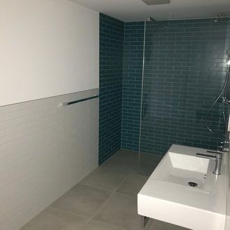 Modernes Badezimmer mit türkisfarbener Fliesendusche, weißem Waschbecken und grauem Boden.