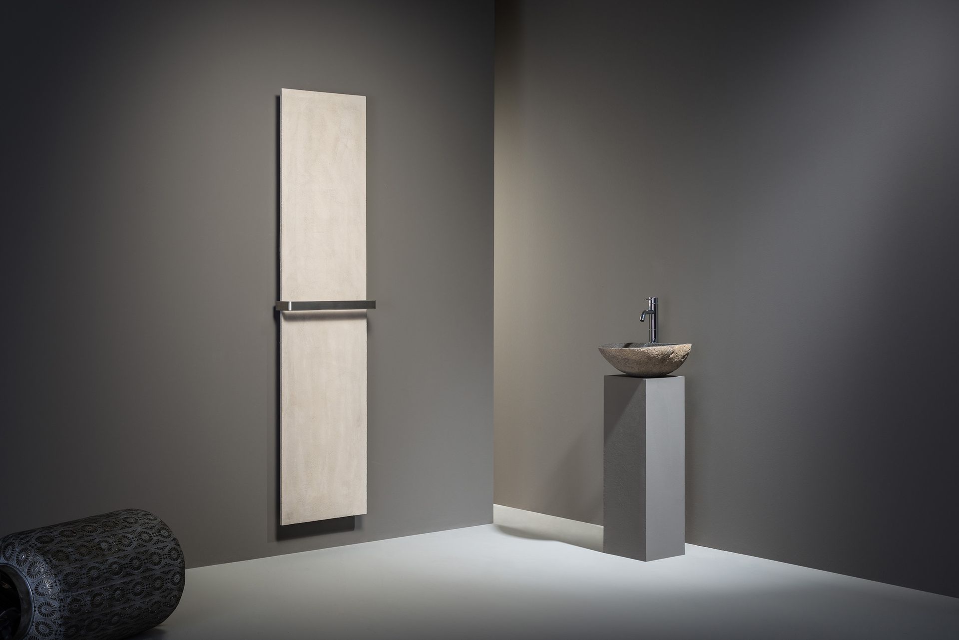 Moderne Badezimmerecke mit hohem beigefarbenem Handtuchwärmer, Steinwaschbecken auf Sockel und dunklen Wänden.