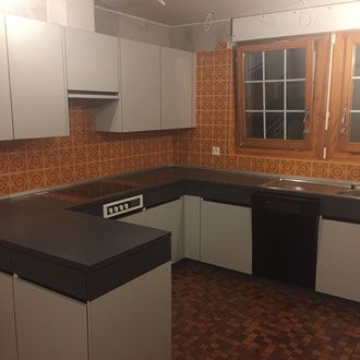 Küche in Grau und Schwarz mit U-förmiger Arbeitsplatte, orangefarbenen Fliesen als Spritzschutz und Holzfenster.