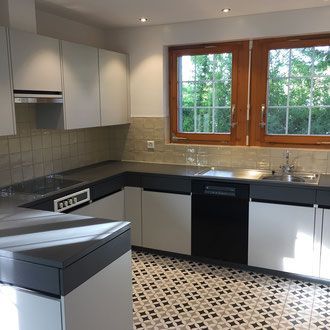 Moderne Küche mit grauen Arbeitsplatten, weißen Schränken, schwarzen Geräten und gemustertem Fliesenboden.