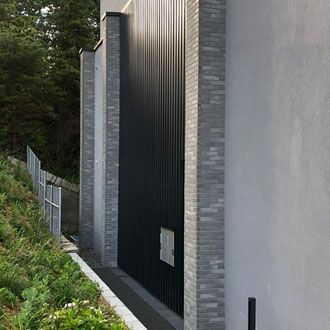 Schwarzes Metalltor mit gemauerten Säulen, die in eine graue Mauer eingelassen sind.