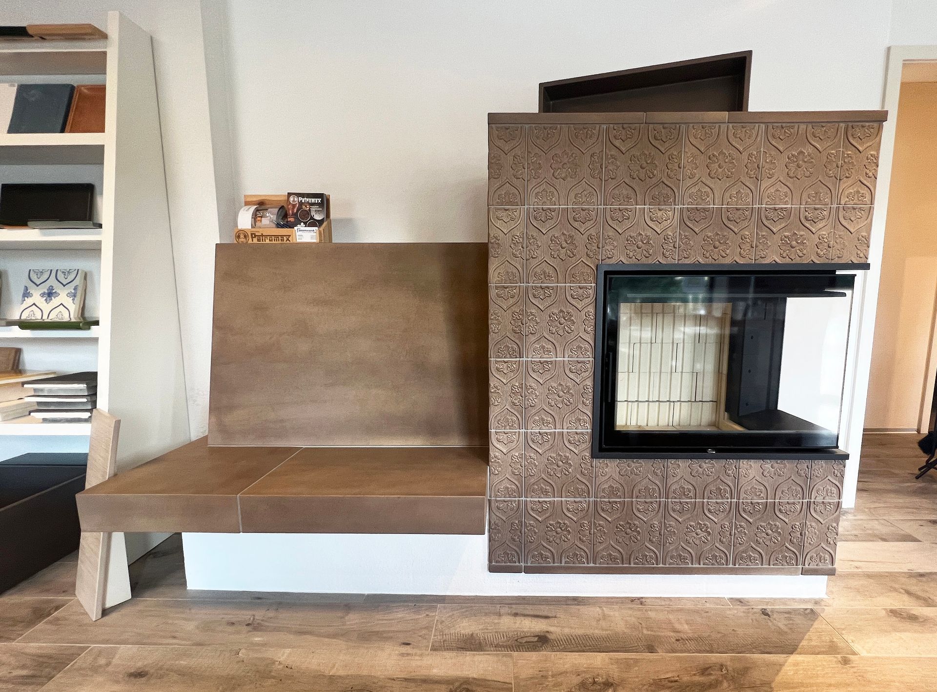 Moderner Kamin mit Sitzbank und gemusterten Fliesen vor einer weißen Wand.