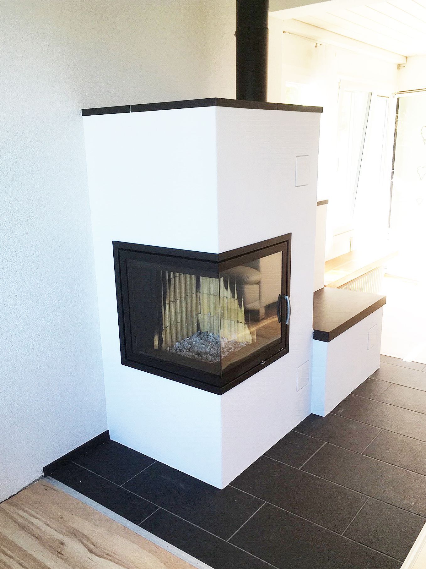 Weißer Eckkamin mit schwarzem Rahmen, Glastür und schwarzem Fliesenboden.