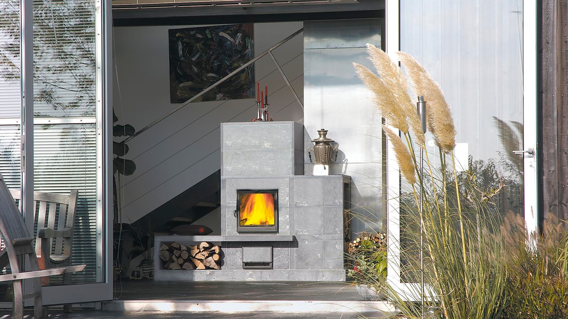 Steinkamin mit brennendem Feuer und Holzvorrat vor dem Hintergrund von Glastüren.