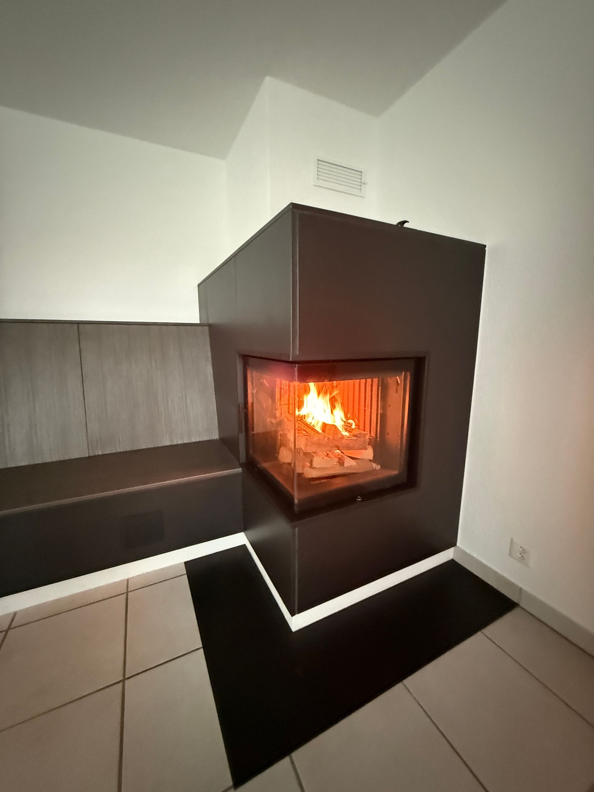 Eine Zimmerecke ist mit rechteckigen, beigen und hellbraunen Steinen gefliest. An einer Wand befindet sich ein dunkler Fleck. Eine Steckdose ist sichtbar.