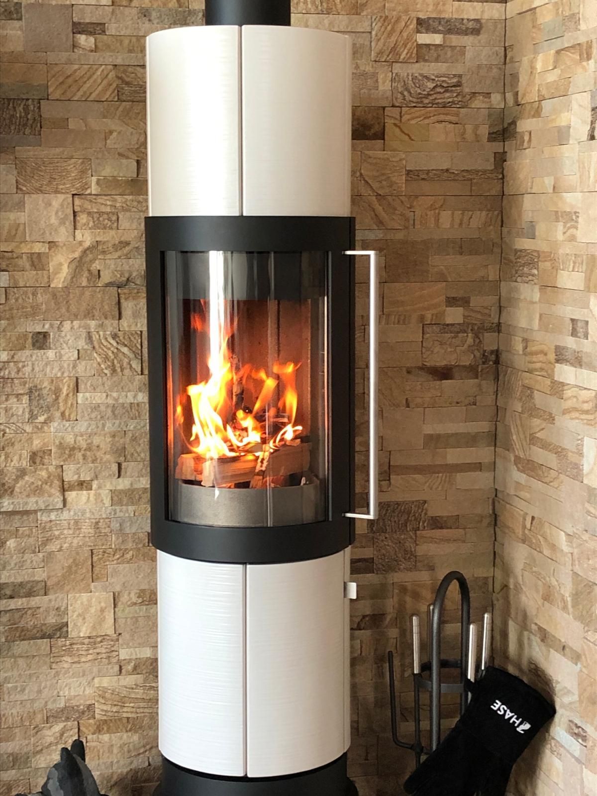 Moderner Kamin in Weiß und Schwarz mit Feuer vor einer Steinwand.