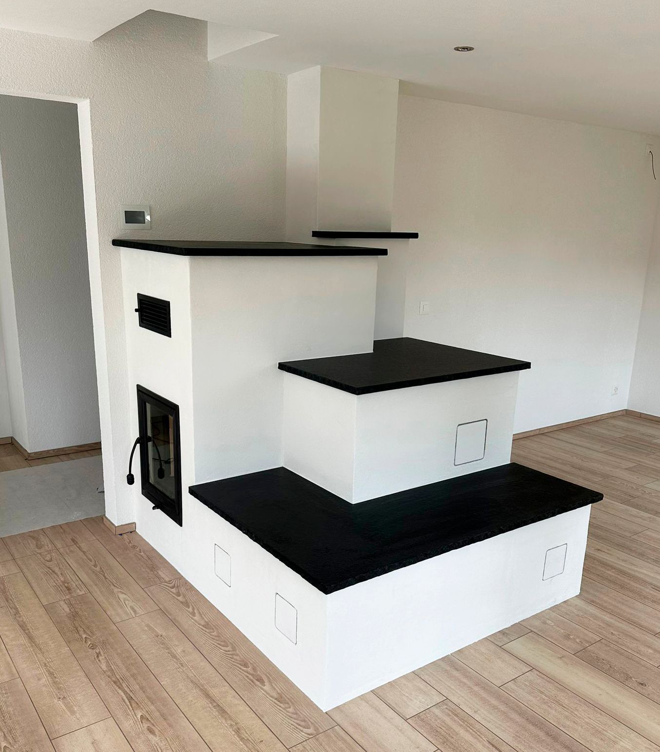 Ein weiß-schwarzer Stufenofen in einem Raum mit hellem Holzboden.