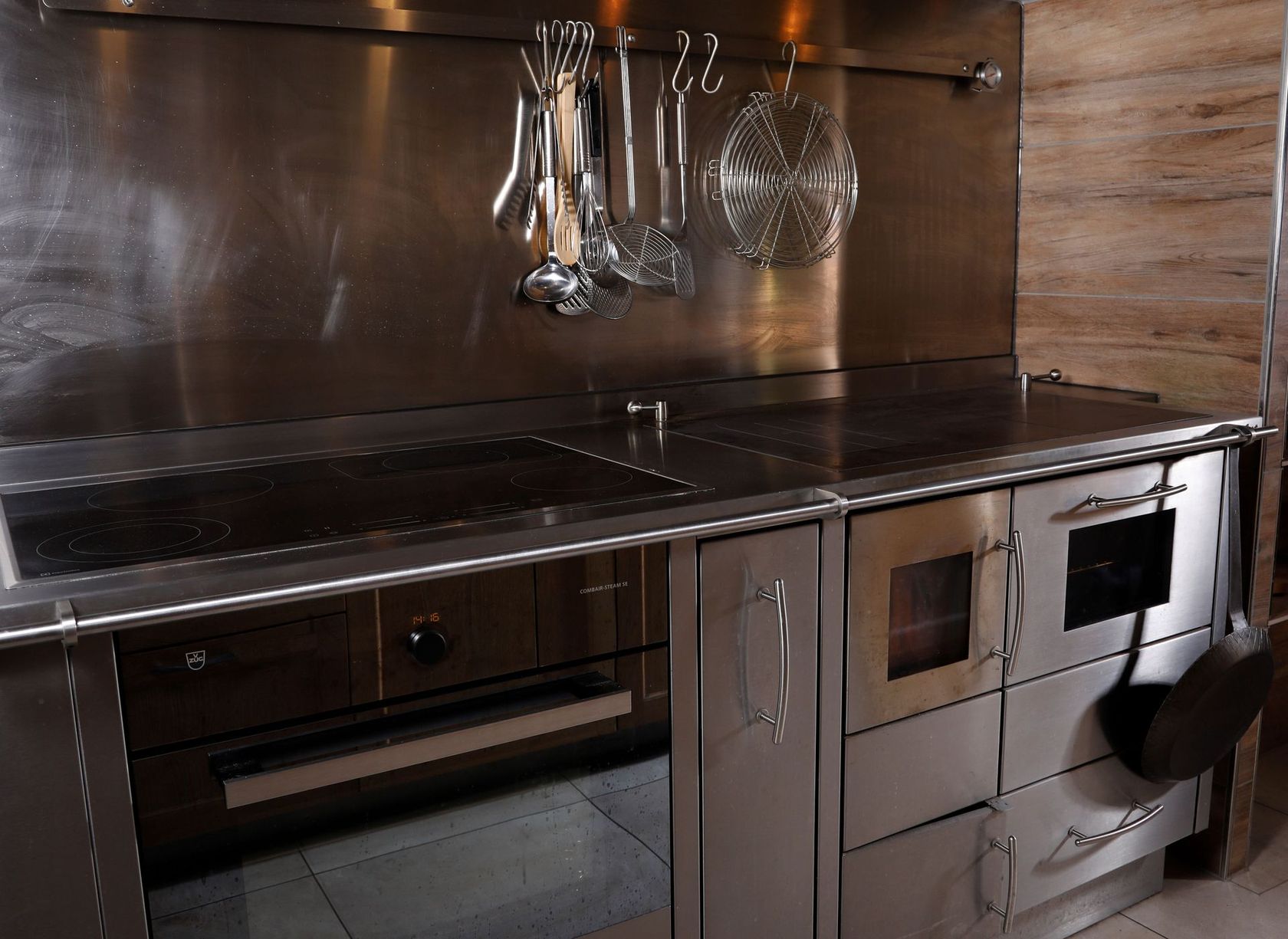 Küchenherd aus Edelstahl mit Backofen, Kochfeld und Hängevorrichtung für Küchenutensilien.