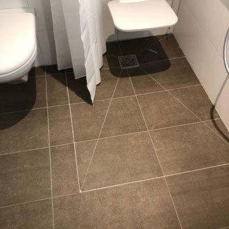 Braun gefliester Badezimmerboden mit Toilette, Duschvorhang und kleiner Toilette.