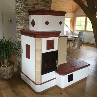 Ein weiß-rot gekachelter Kamin mit schwarzer Tür in einem Zimmer mit Holzboden.