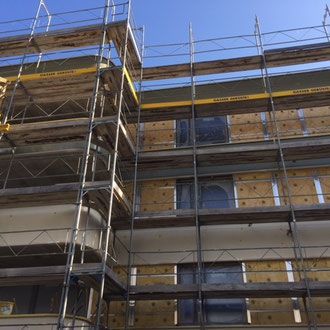 Gerüst an einem Wohnhaus, das renoviert wird; blauer Himmel im Hintergrund.