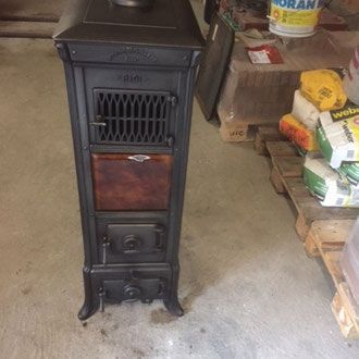 Schwarzer gusseiserner Holzofen mit kunstvollen Verzierungen, aufgestellt in einem Innenraum in der Nähe von Baumaterialien.