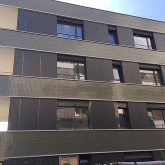 Modernes Apartmentgebäude mit dunkelgrauen Paneelen, Fenstern und hellbraunen Akzenten.