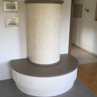 Ein weiß-grau gekachelter Ofen in einem Raum mit gerahmten Kunstwerken an der Wand und Holzboden.