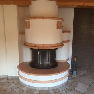 Kamin aus weißen und hellbraunen Ziegeln mit rundem Sockel, Feuerstelle und Schornstein auf gefliestem Boden.