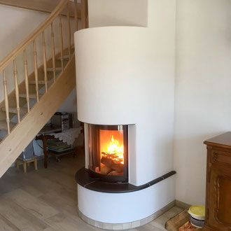 Weißer Kamin mit brennendem Feuer, neben einer Holztreppe und einem Holzschrank.
