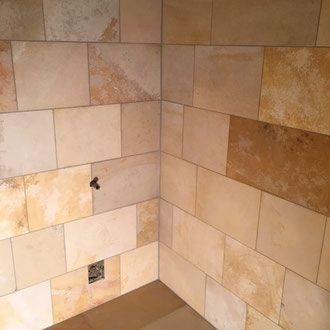 Eine Zimmerecke ist mit rechteckigen, beigen und hellbraunen Steinen gefliest. An einer Wand befindet sich ein dunkler Fleck. Eine Steckdose ist sichtbar.