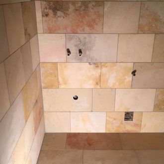 Duschkabine mit Steinfliesen, freiliegenden Sanitärarmaturen und Elektroverteilerkasten.