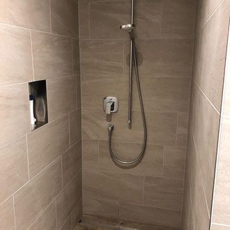 Dusche mit beigefarbenen Fliesen, Duschkopf, Wasserhahn und eingelassenem Seifenspender.