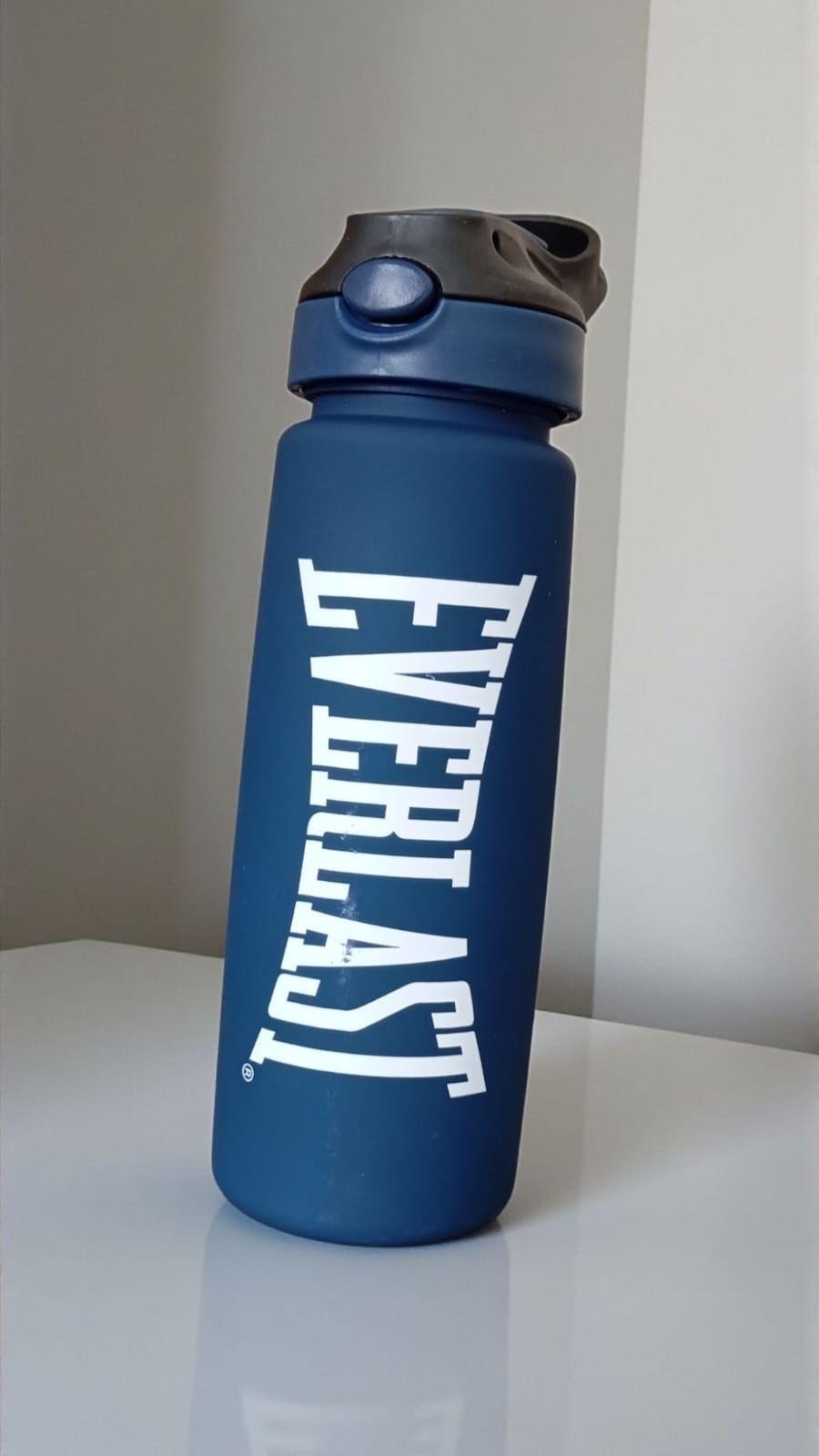 Botella de agua Everlast azul sobre una superficie blanca con fondo gris.