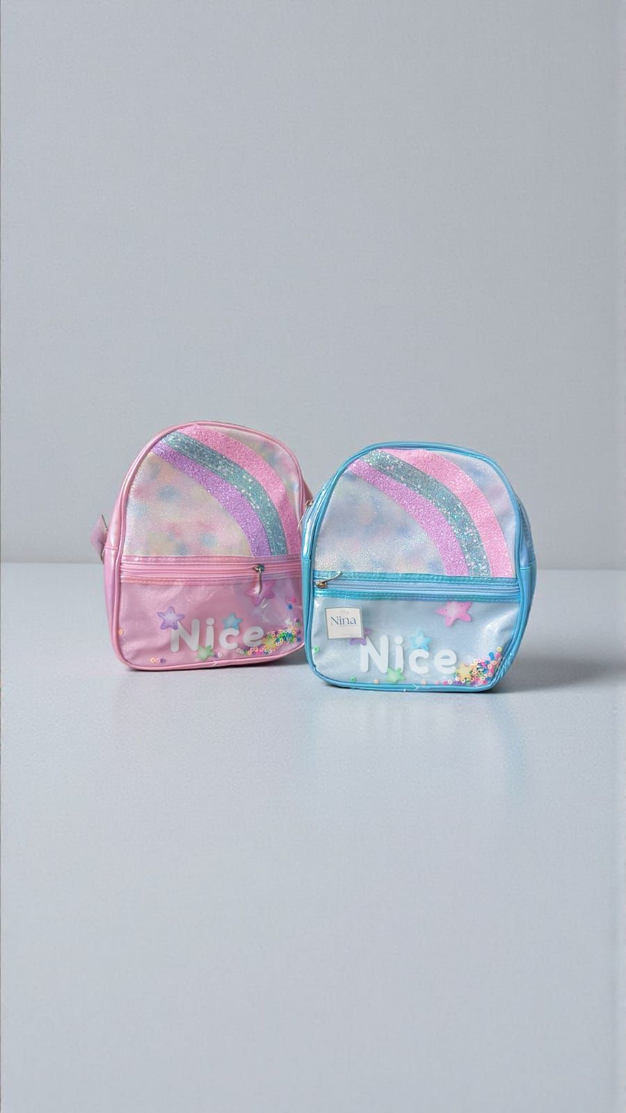 Dos mochilas pequeñas y coloridas. Una rosa y otra azul, con estampado de arcoíris y la palabra