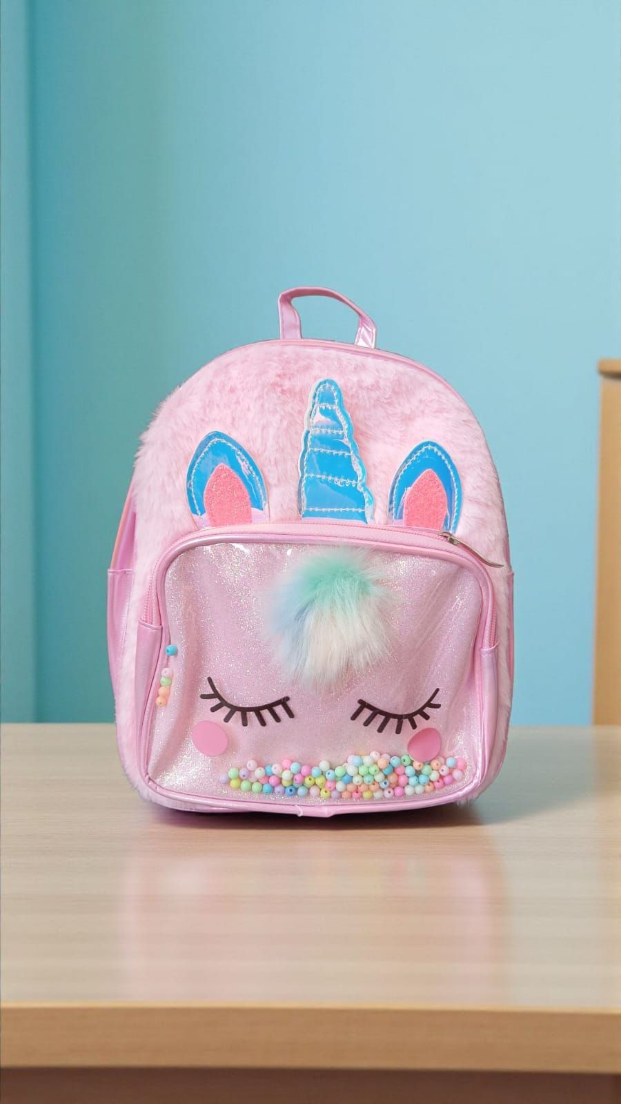 Mochila rosa de unicornio sobre un escritorio, con una carita brillante y pelaje esponjoso.