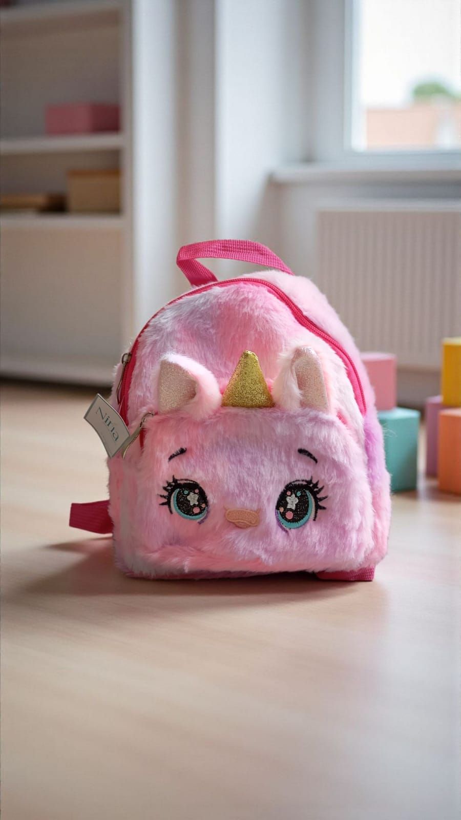 Mochila rosa de unicornio sobre un suelo de madera, con bloques de colores al fondo.
