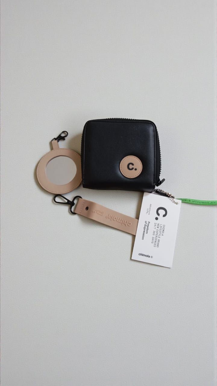 Cartera negra con etiqueta circular color canela y llavero sobre fondo blanco.