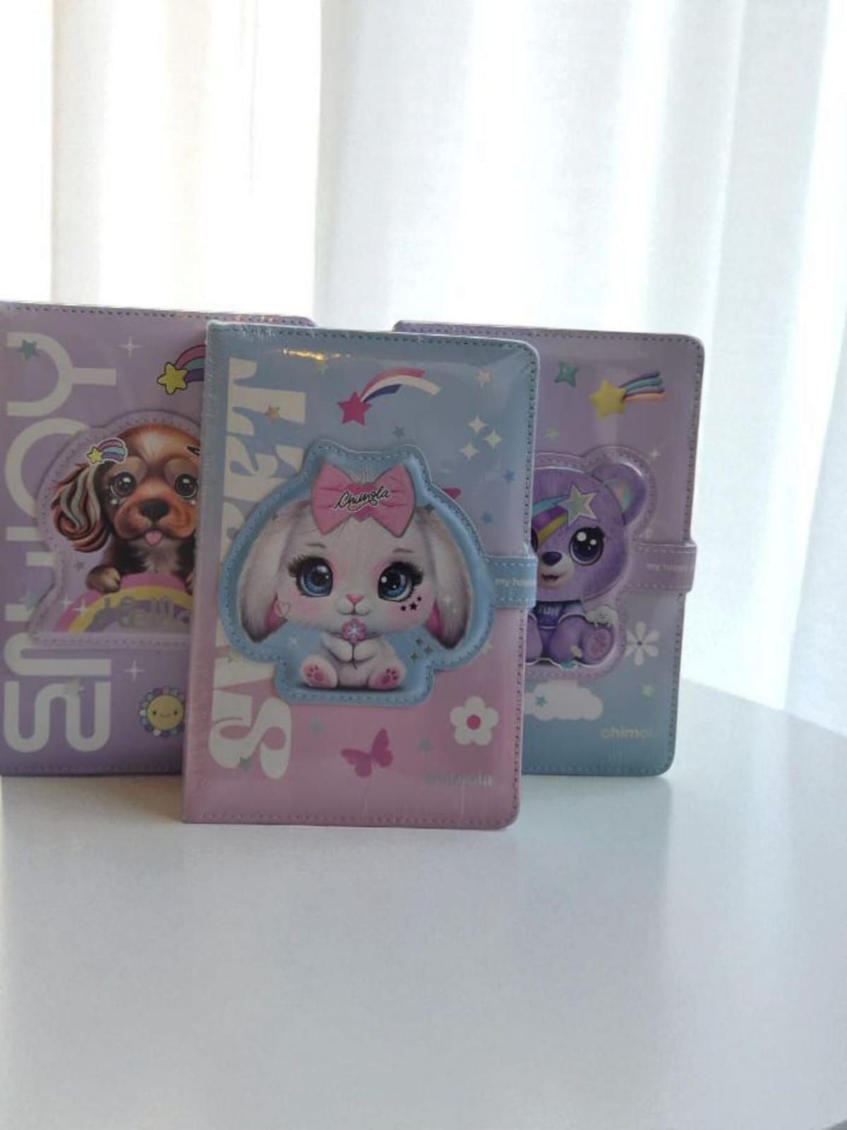 Tres cuadernos de colores pastel con diseños de animales: perro, conejo y oso, sobre fondo blanco.