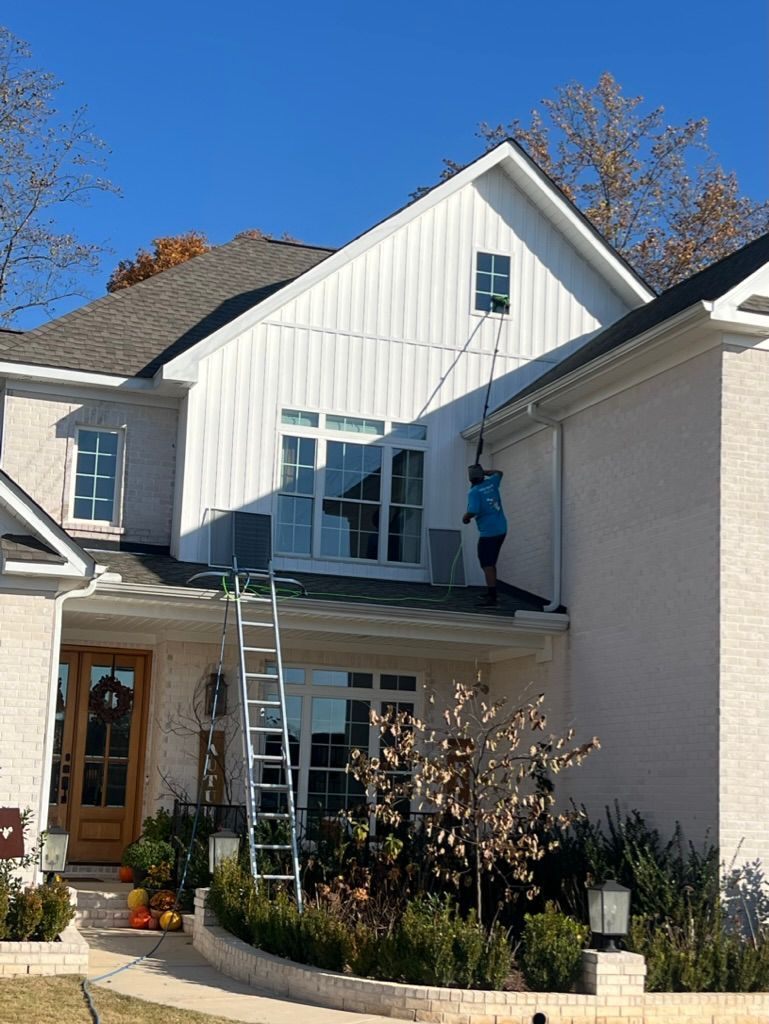 Worker on ladder painting the upper exterior of a white house on a sunny day