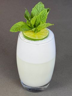 A glass of white liquid with a lime slice and mint leaves on top.