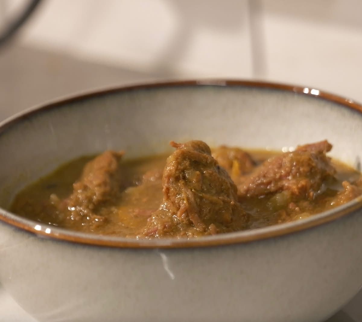 Bowl of goat curry with visible chunks of meat in a thick, brownish gravy.