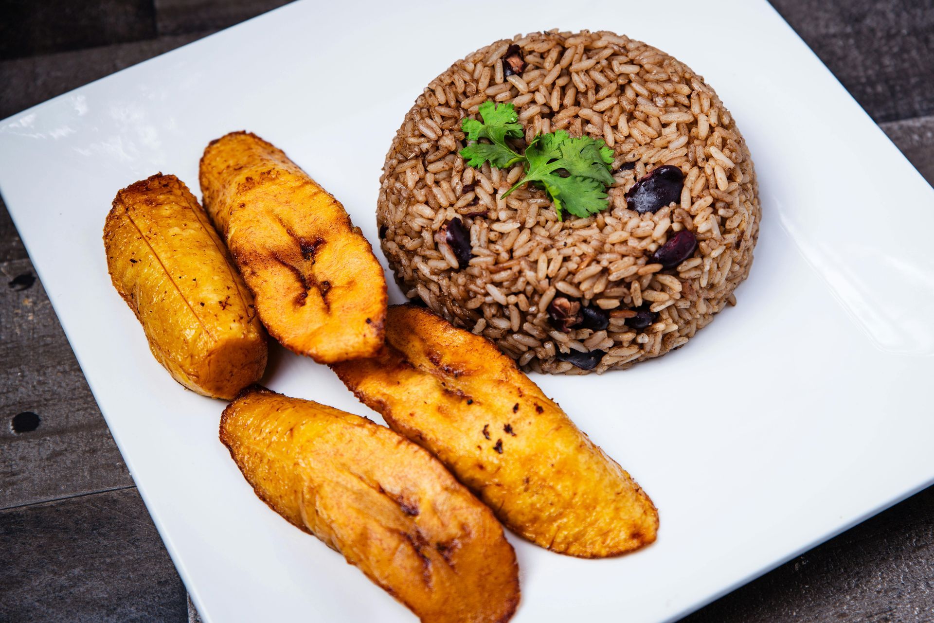 Fried plantains and rice with beans on a white plate.
