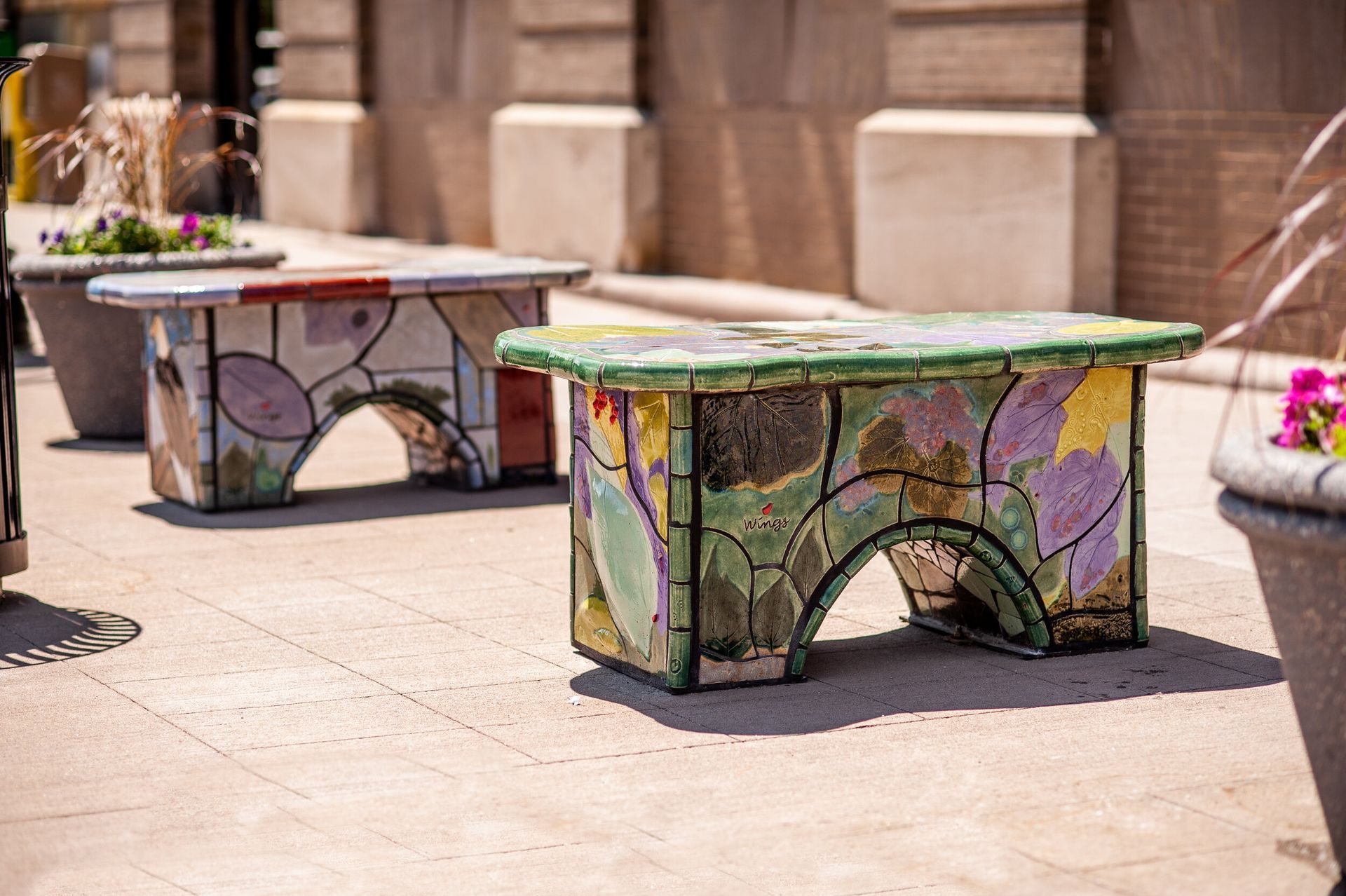 A row of colorful benches are sitting on a sidewalk in front of a building.
