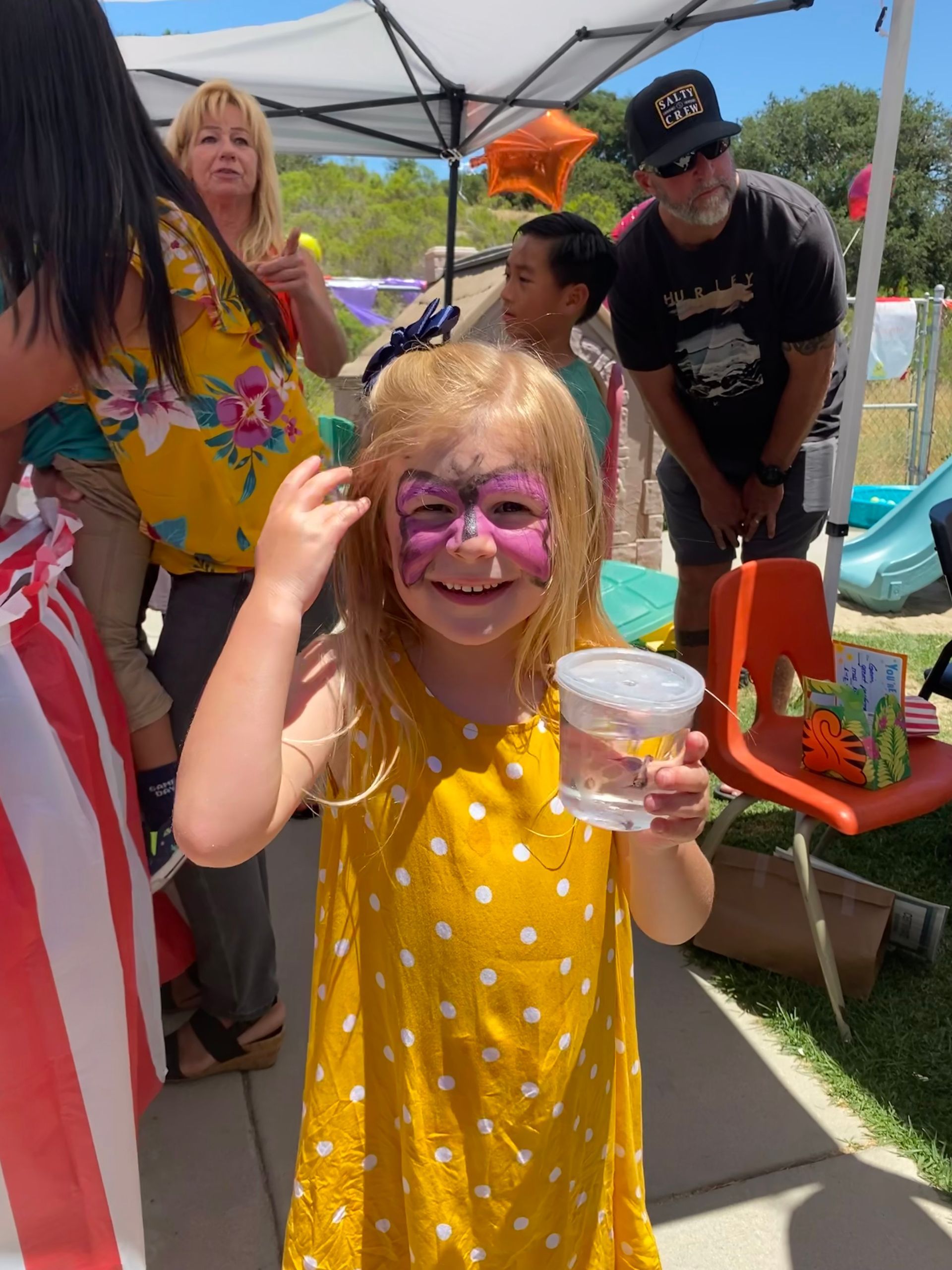 A little girl with her face painted holding a cup of water.
