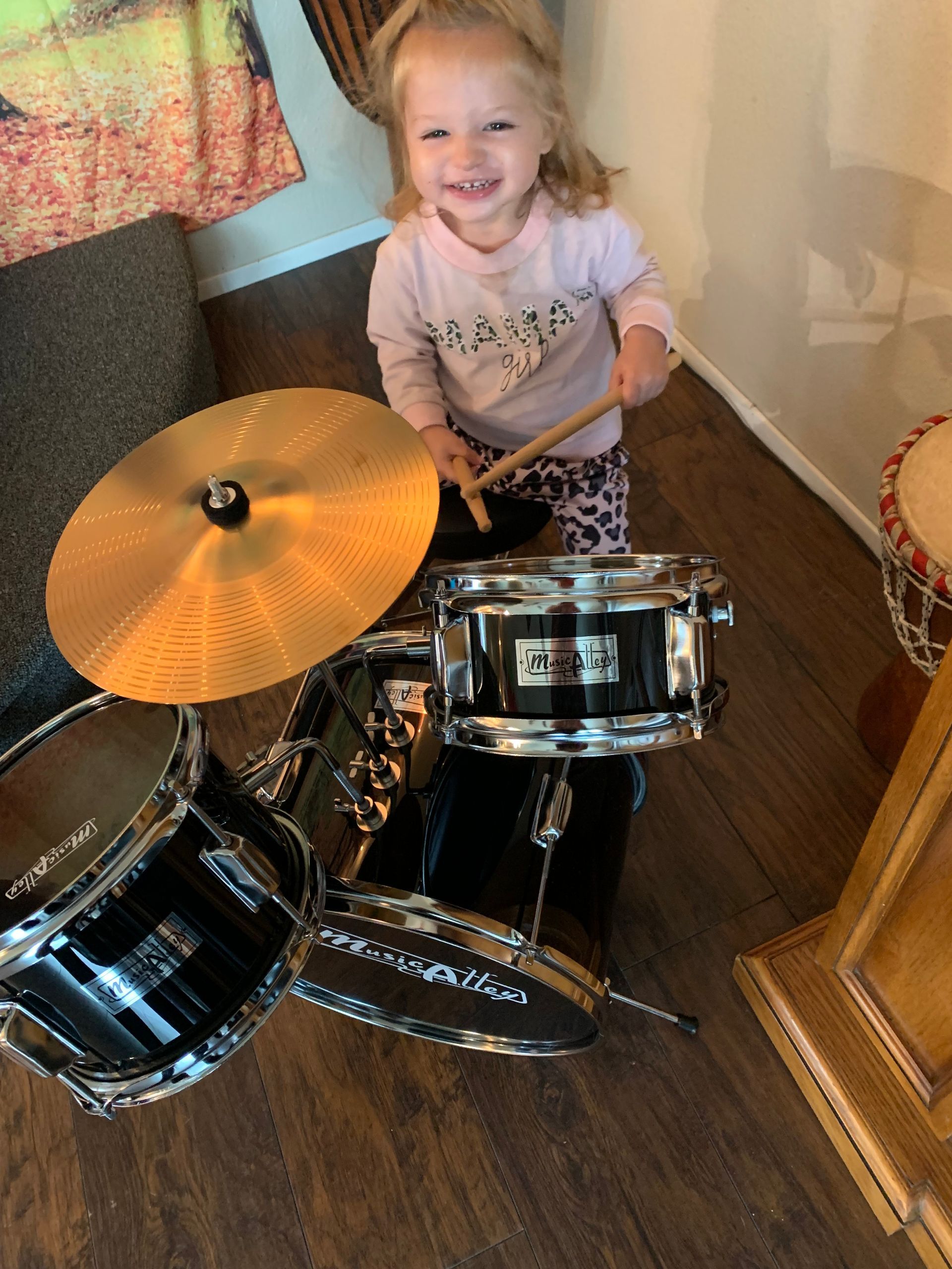 A little girl is playing a drum set in a living room.