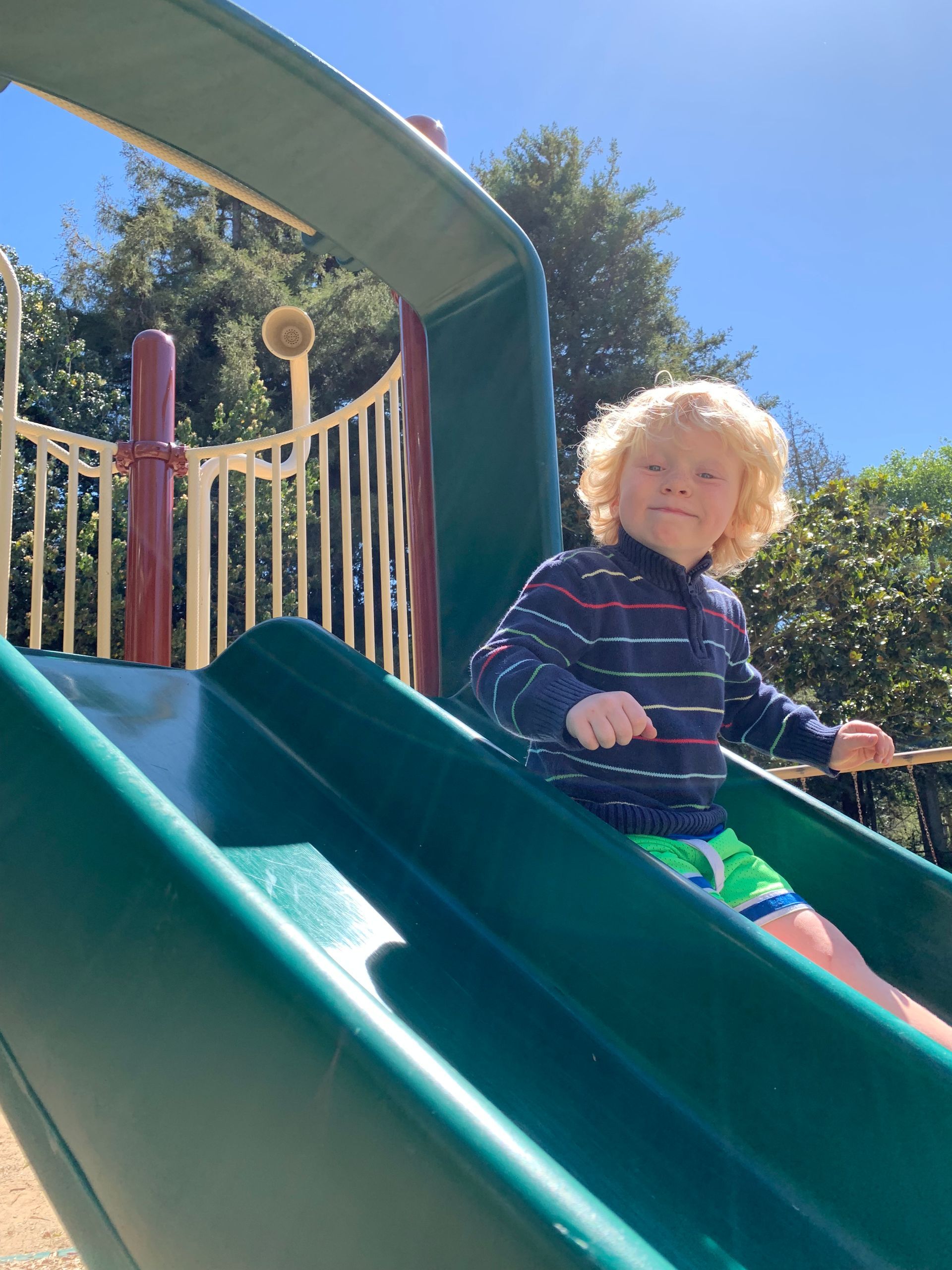 A young boy is riding down a slide at a playground.