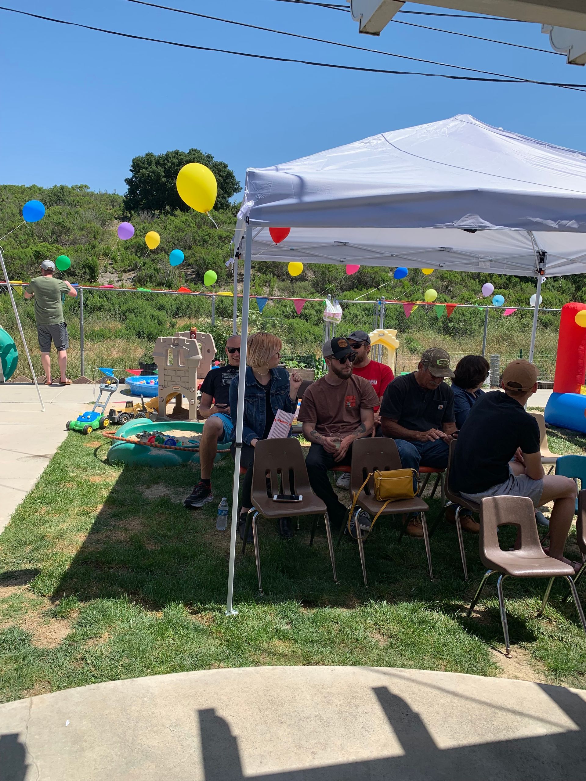 A group of people are sitting under a tent with balloons hanging from it.
