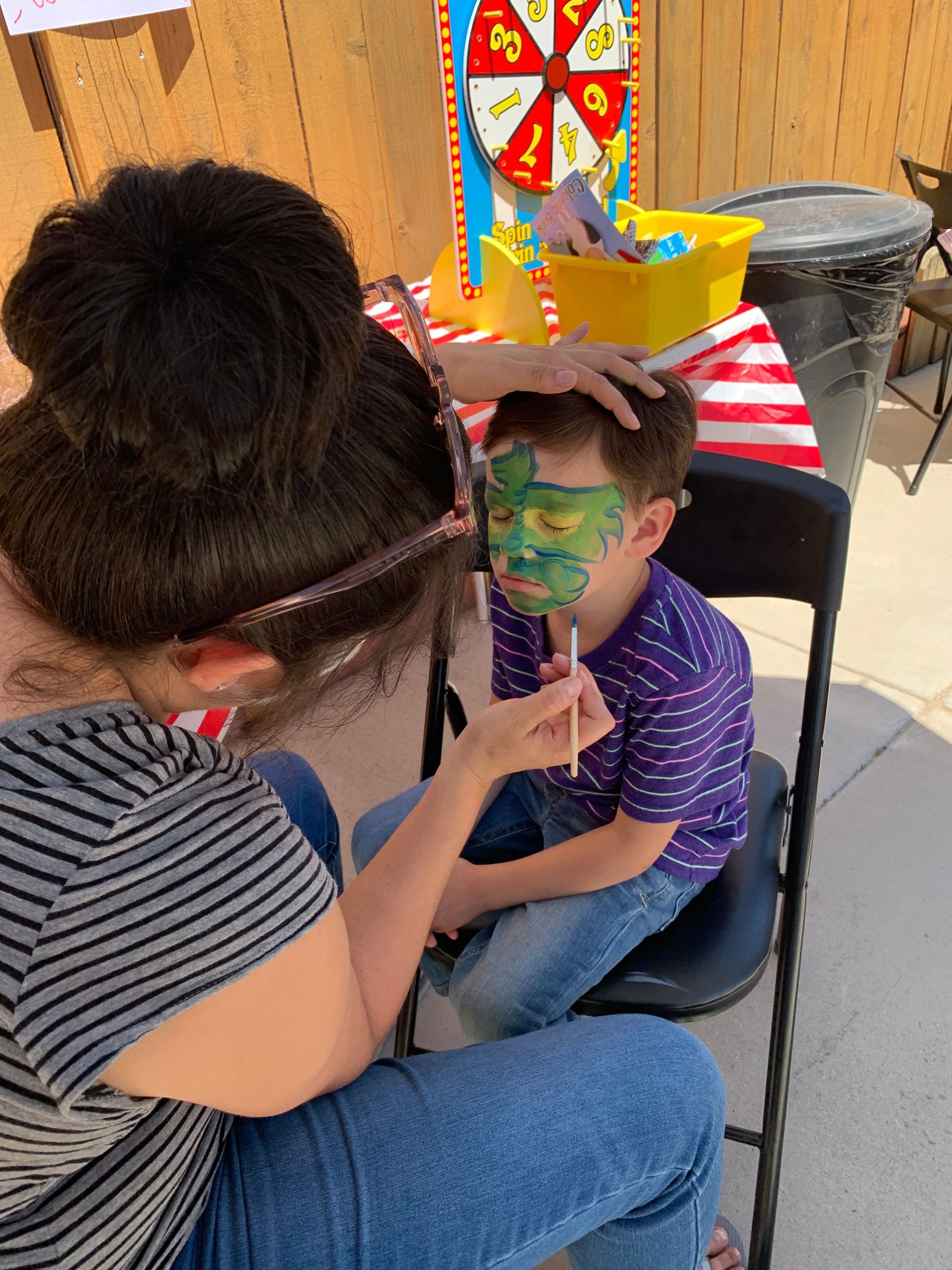 A woman is painting a child 's face with a green mask