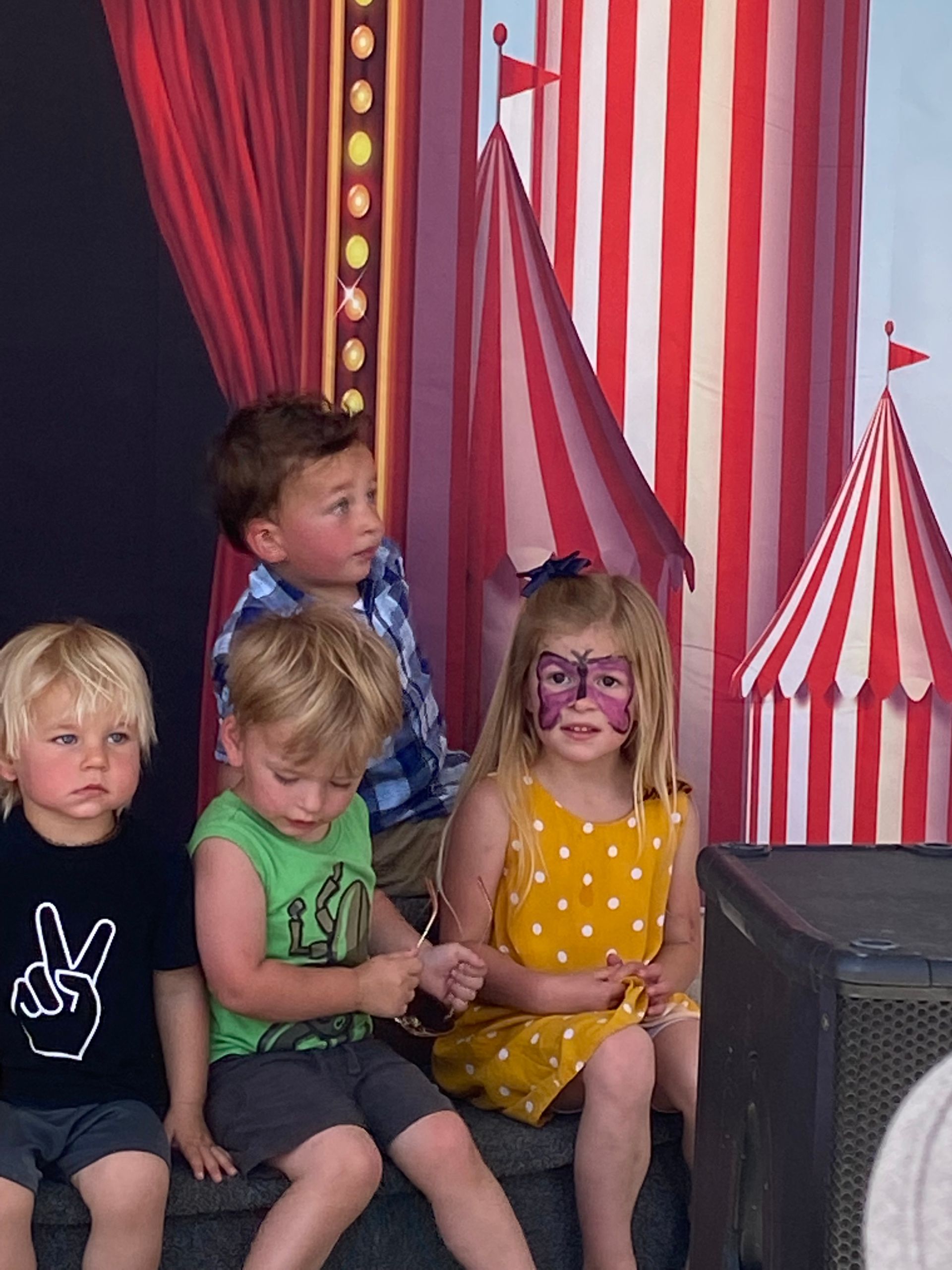 A group of children are sitting in front of a carnival backdrop.