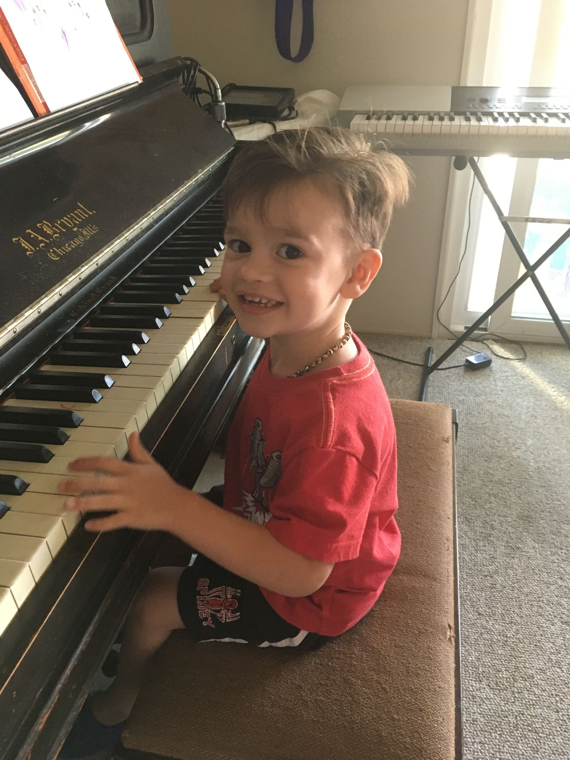 A young boy in a red shirt is playing a piano